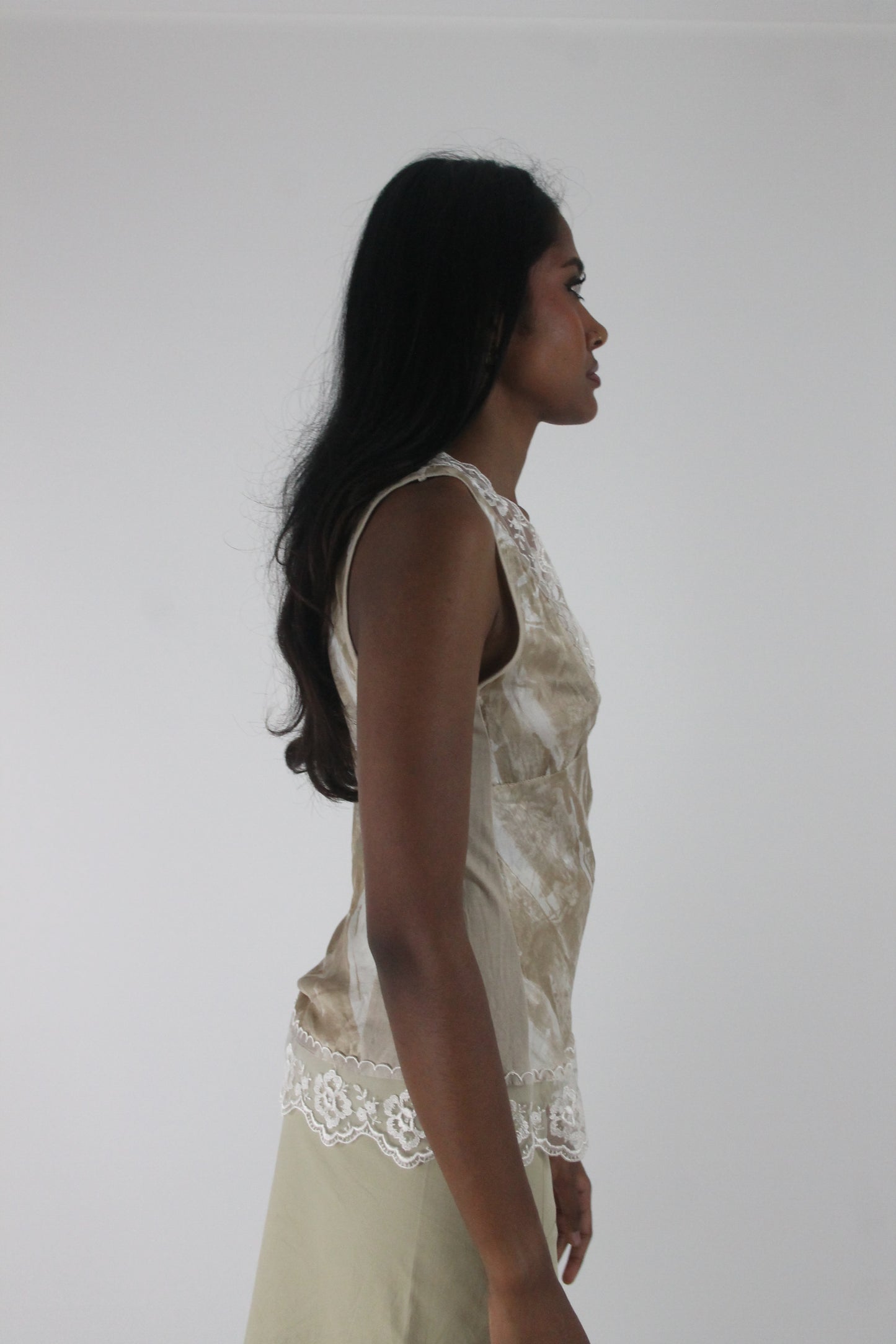 side view of small cream satin-effect sleeveless top with white lace trim