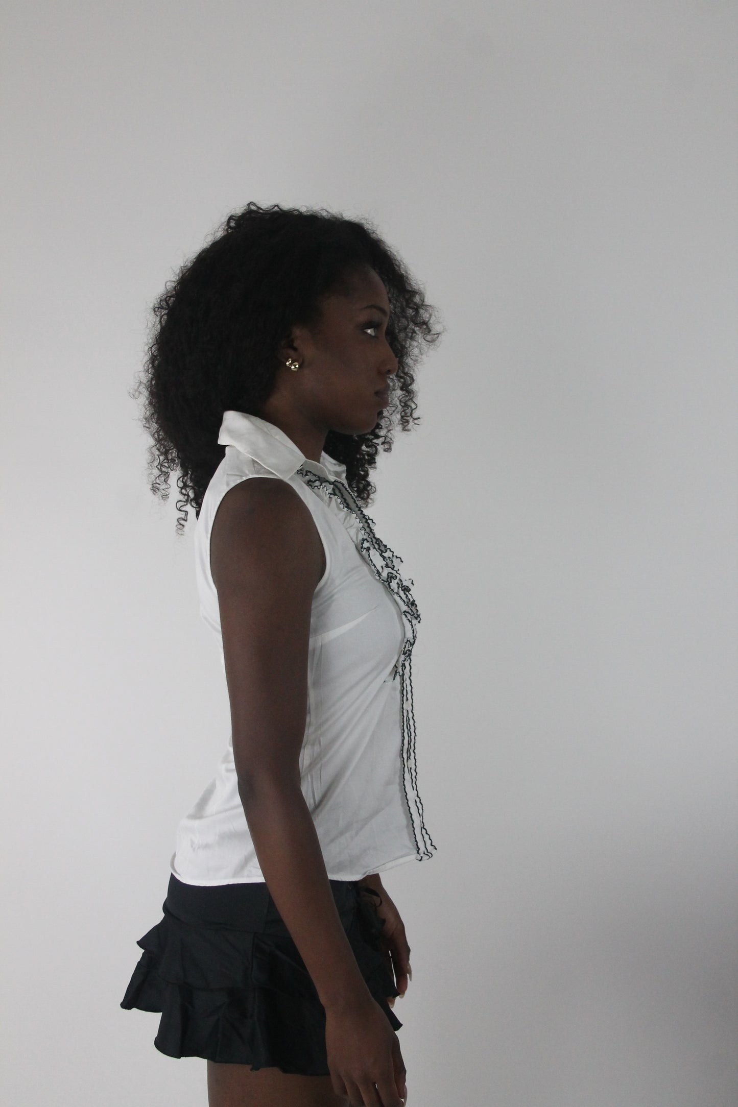alternate-side view of white sleeveless collared shirt with black piping